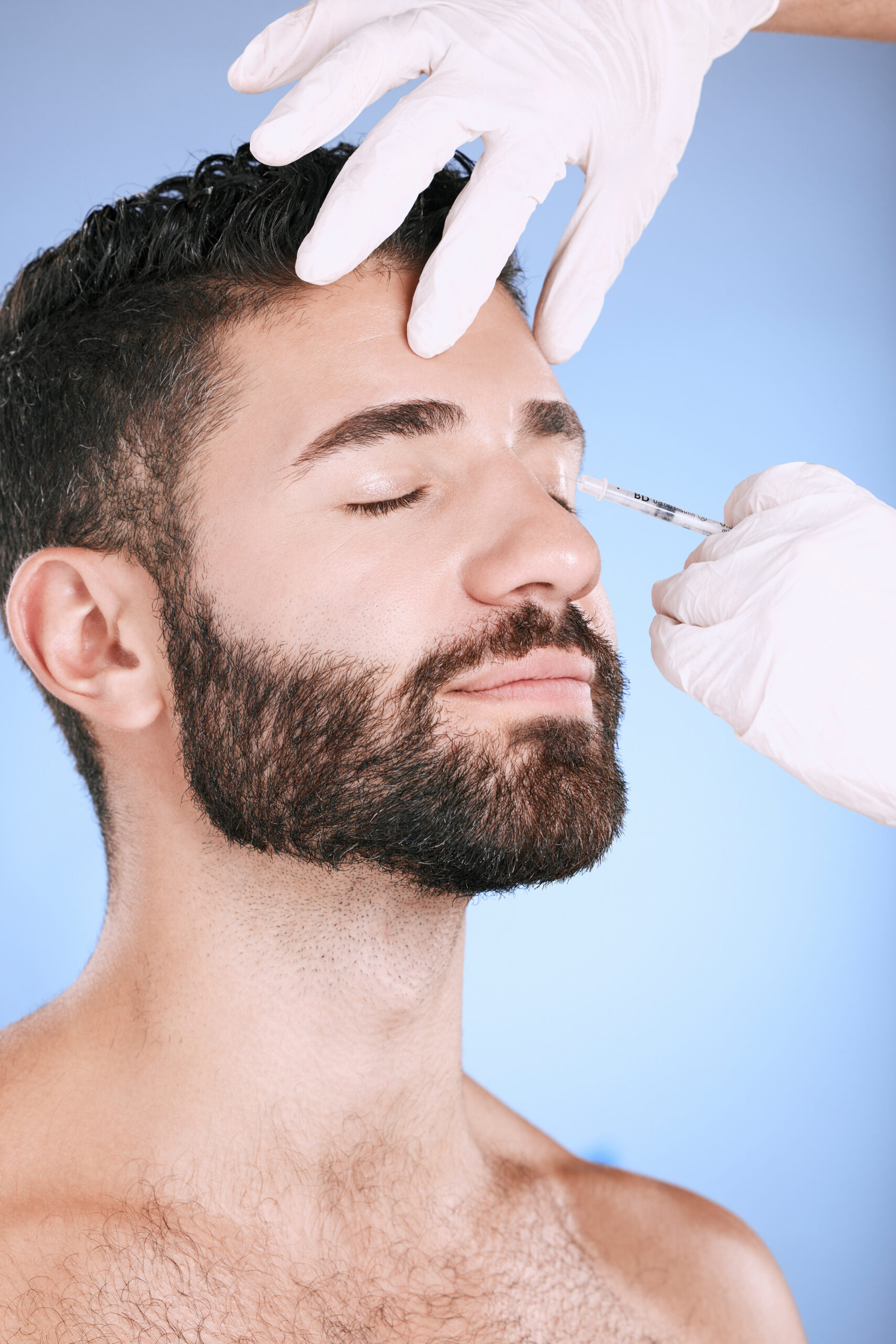 Injection, man and studio for skincare, collagen wellness and beauty process at salon. Cosmetics, face and needle of plastic surgery, botox and facial change of aesthetic prp, eyes or blue background.