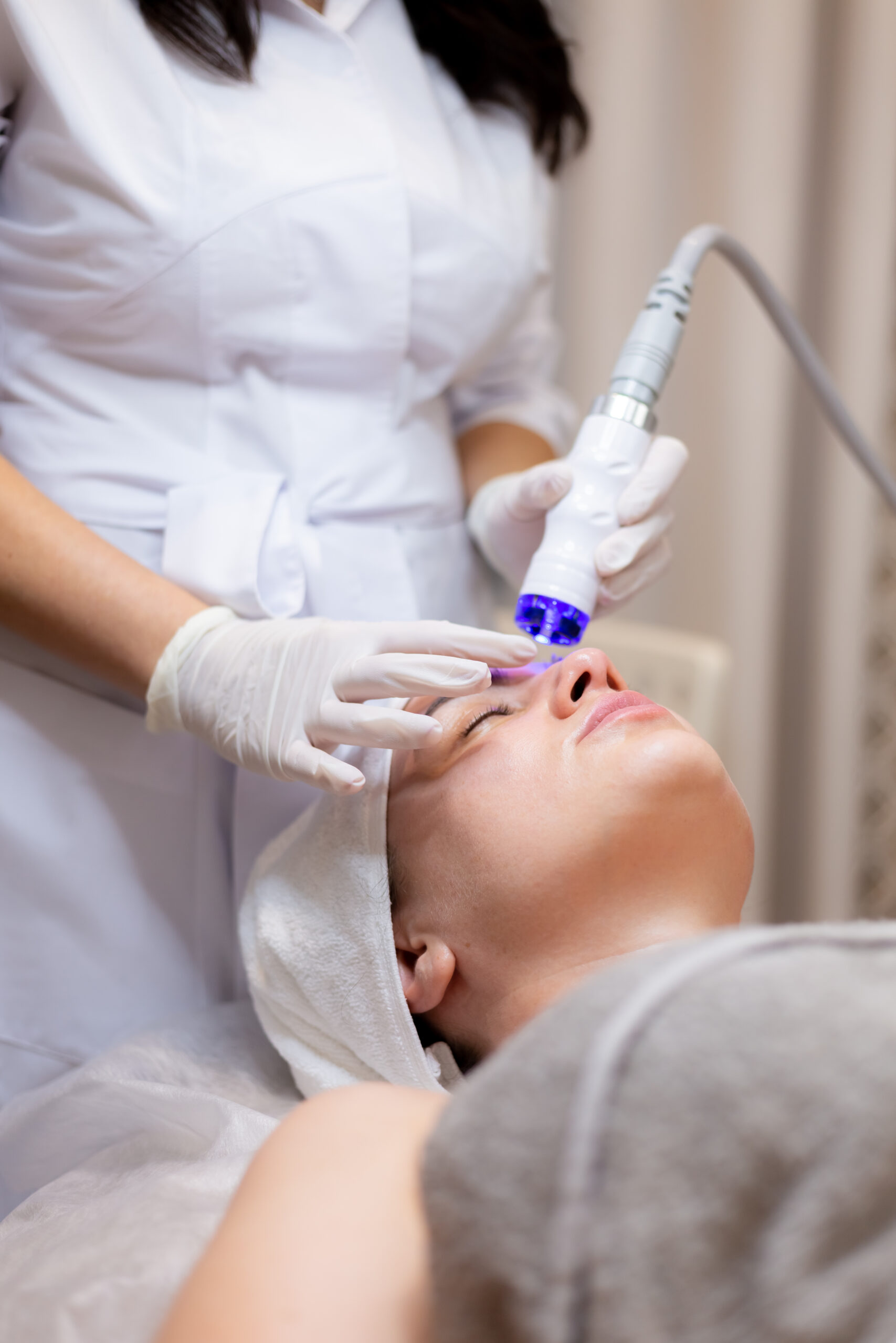 A young beautiful girl lies on the beautician's table and receives procedures with a professional apparatus for skin rejuvenation and moisturizing