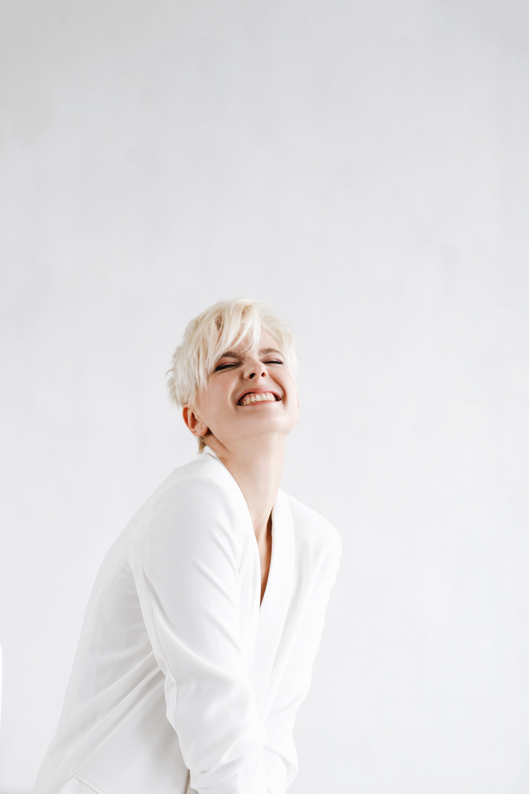 Woman in white suit looks funny posing before a white wall
